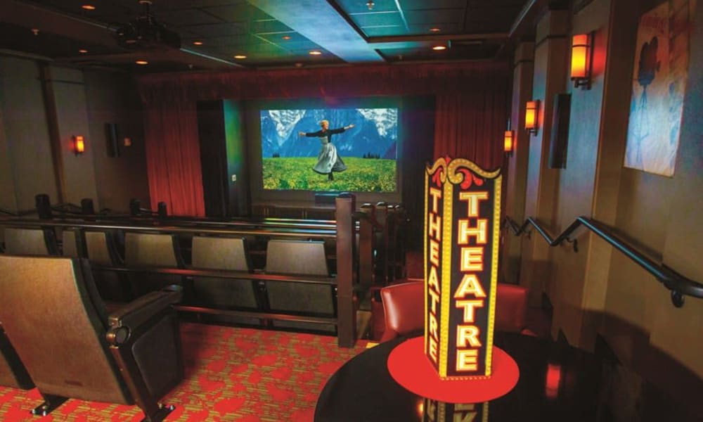 A cozy home theater with red carpet, plush seating, and wall sconces showing a scene from 