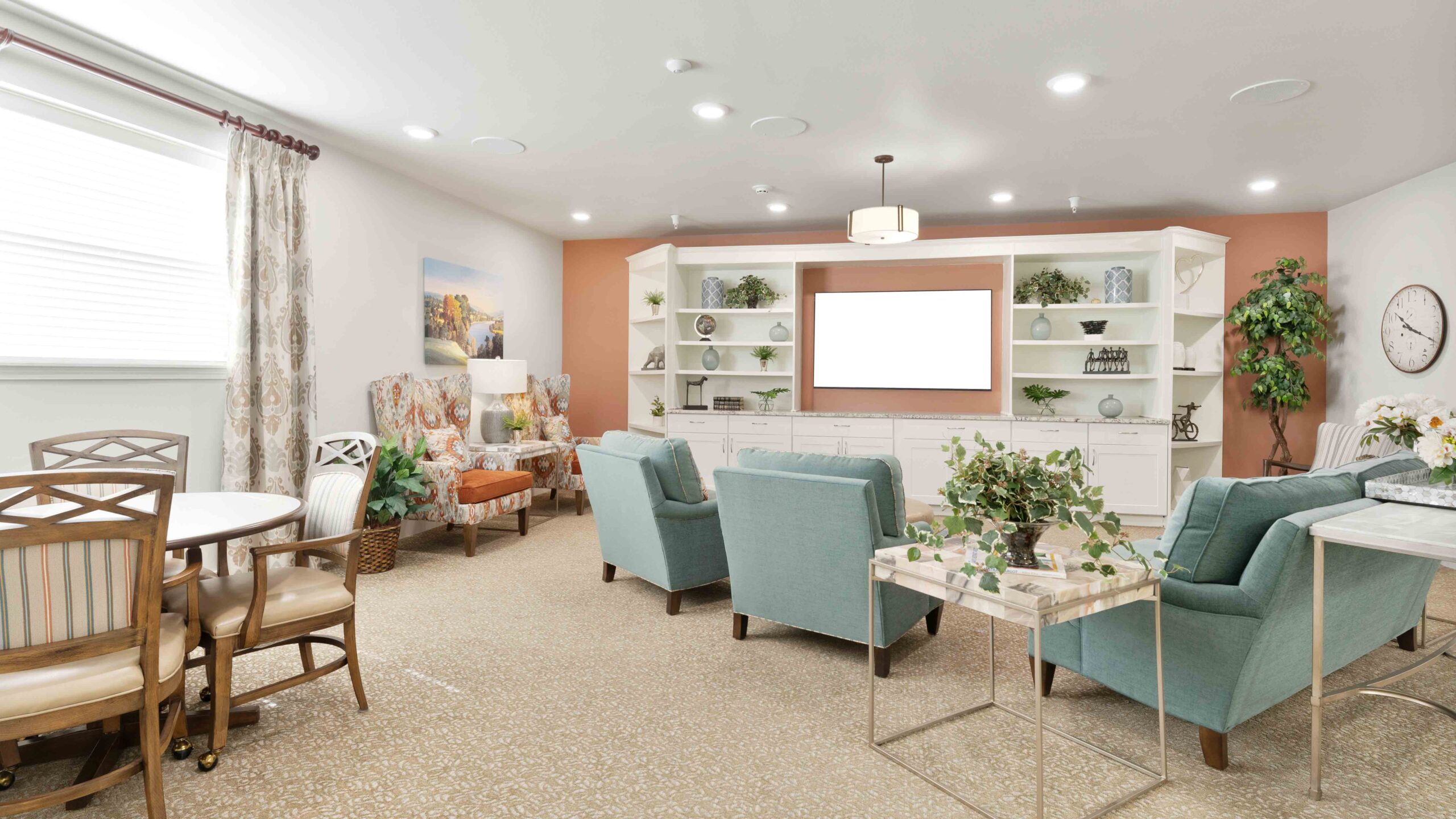 A bright, inviting living room with light blue armchairs, a round table with wooden chairs, built-in shelves with decor, a large TV, and neutral carpeting. Plants and artworks add a cozy, welcoming touch.