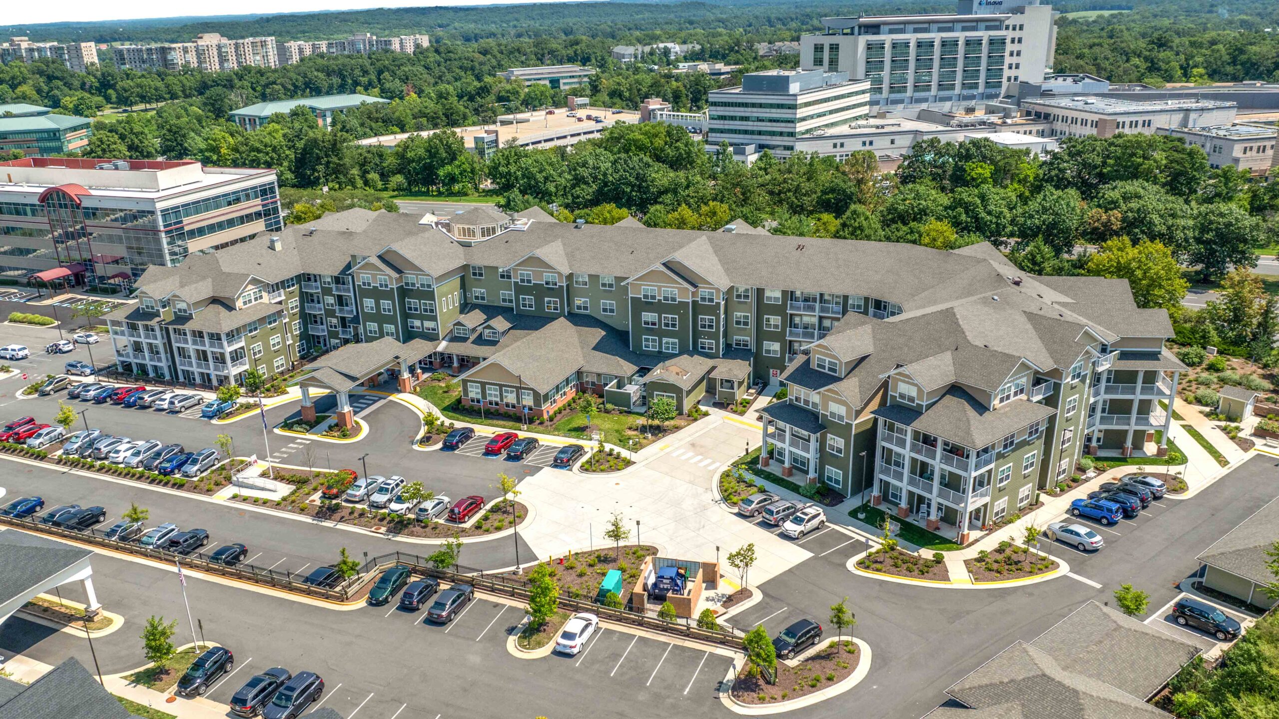 Aerial view of a large modern apartment complex with surrounding parking lots, landscaped greenery, and several nearby office buildings in a suburban area.