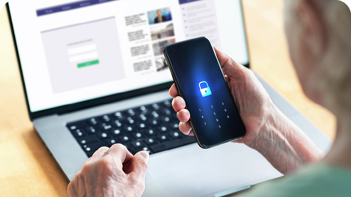 Senior holding smart phone using laptop