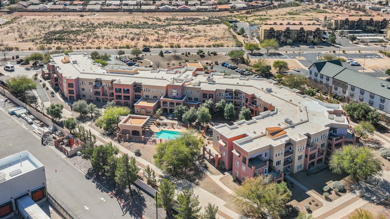 An aerial view of a U-shaped apartment complex with a courtyard pool. Homes are visible in the background.