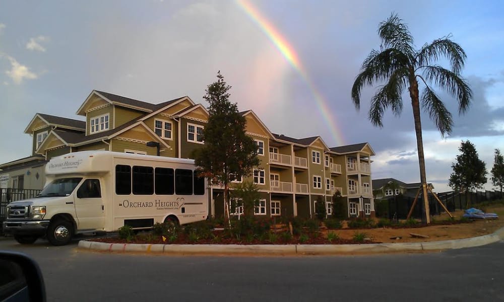 A multi-story residential building with beige and cream siding, surrounded by trees and landscaping. A white van labeled 