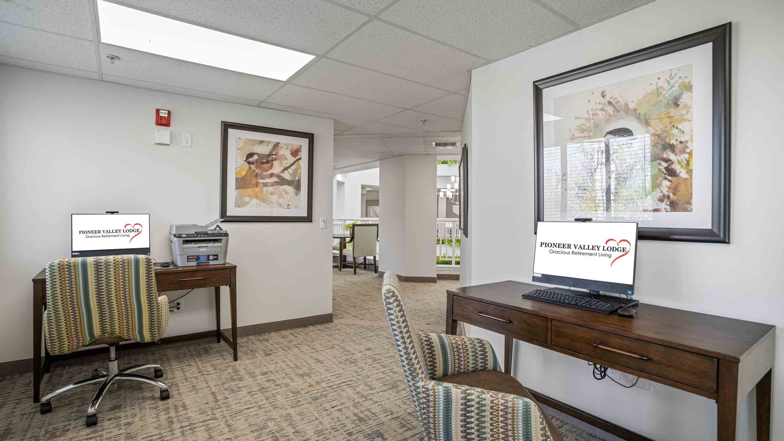 A small office area with two wooden desks, each equipped with a computer displaying 