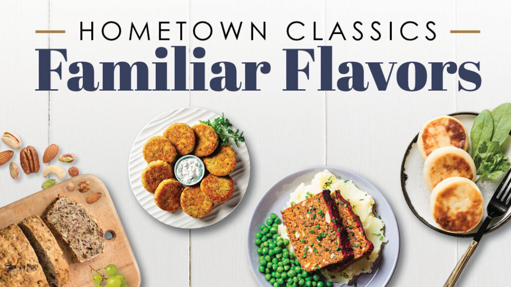An overhead view of classic comfort foods: nut bread, falafel with dip, meatloaf with peas and mashed potatoes, and English muffins with spinach, on a white wooden table. Text reads “Hometown Classics Familiar Flavors.”.