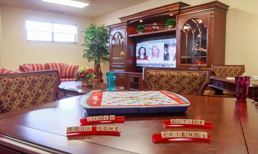 A cozy living room features a Scrabble game in progress on a wooden table. On the tiles are words like 