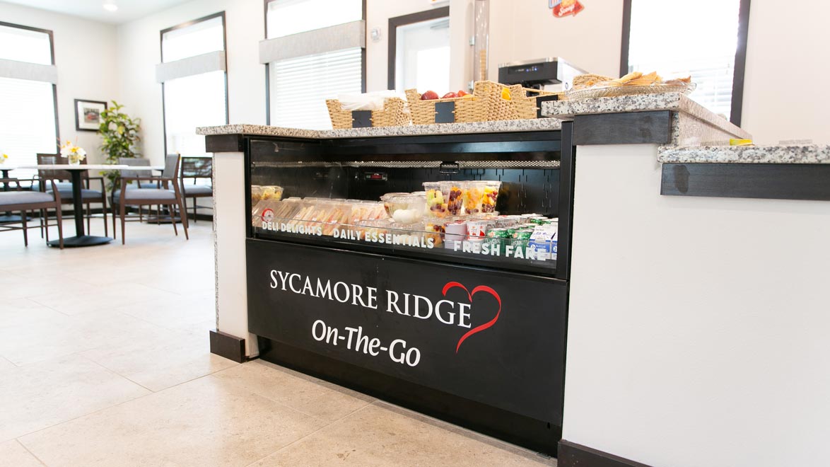 Photo of a small convenience store at Sycamore Ridge, featuring snacks, cold drinks, and fresh fruit. The counter has a sign reading 