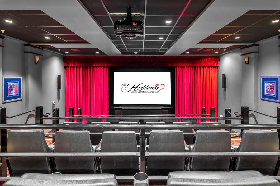 A modern, empty movie theater with stadium-style seating, gray chairs, and red curtains framing the screen. The screen displays the text 