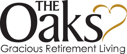 Logo for The Oaks Gracious Retirement Living. The word "Oaks" is prominently featured in bold black letters with a stylized yellow heart shape integrated into the letter "k". The phrases "THE" and "Gracious Retirement Living" are written above and below "Oaks" respectively.