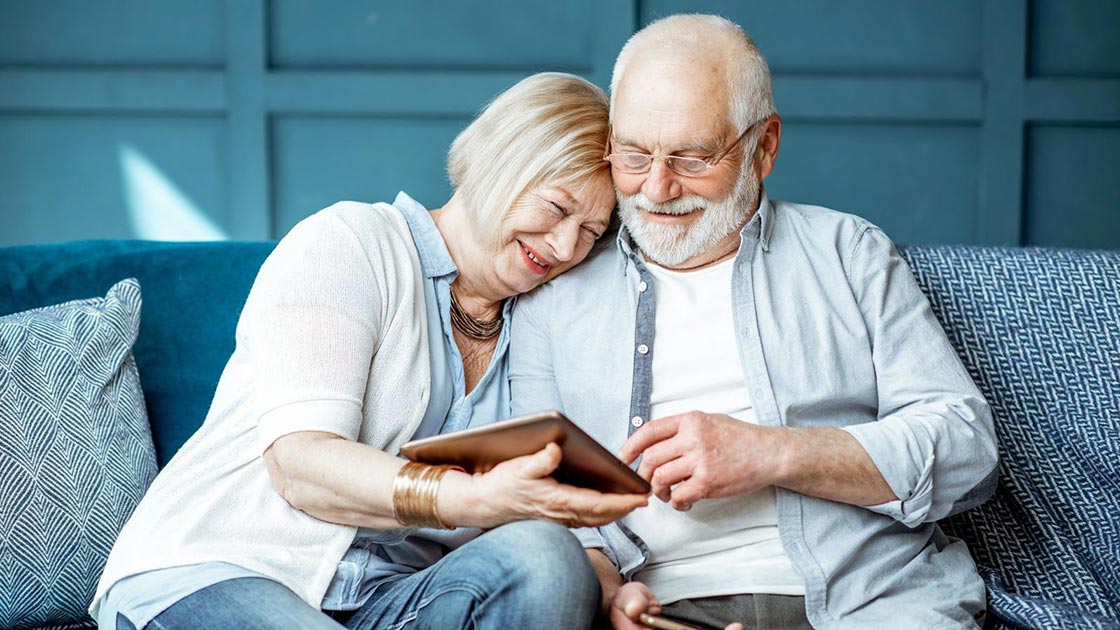 Senior couple sitting on blue couch with ipad