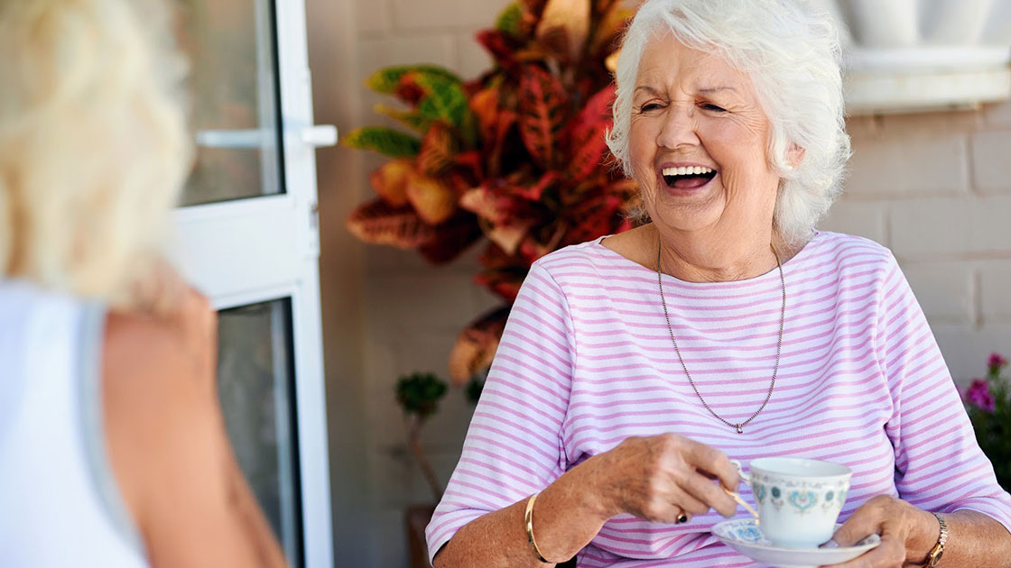 Senior laughing and drinking coffee on porch