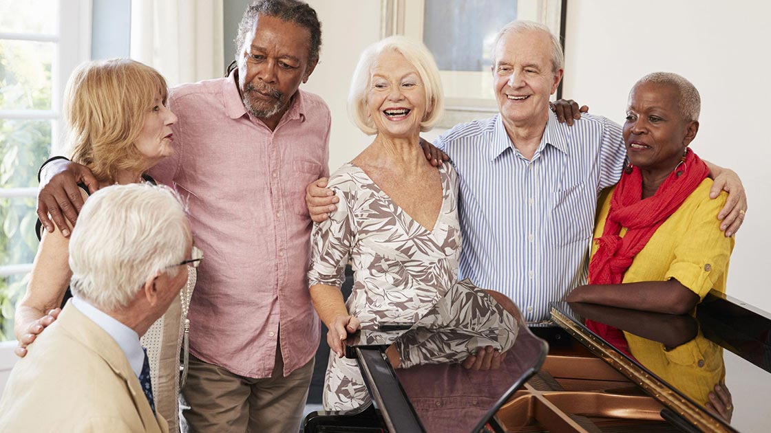 Group of friends standing around a senior playing piano