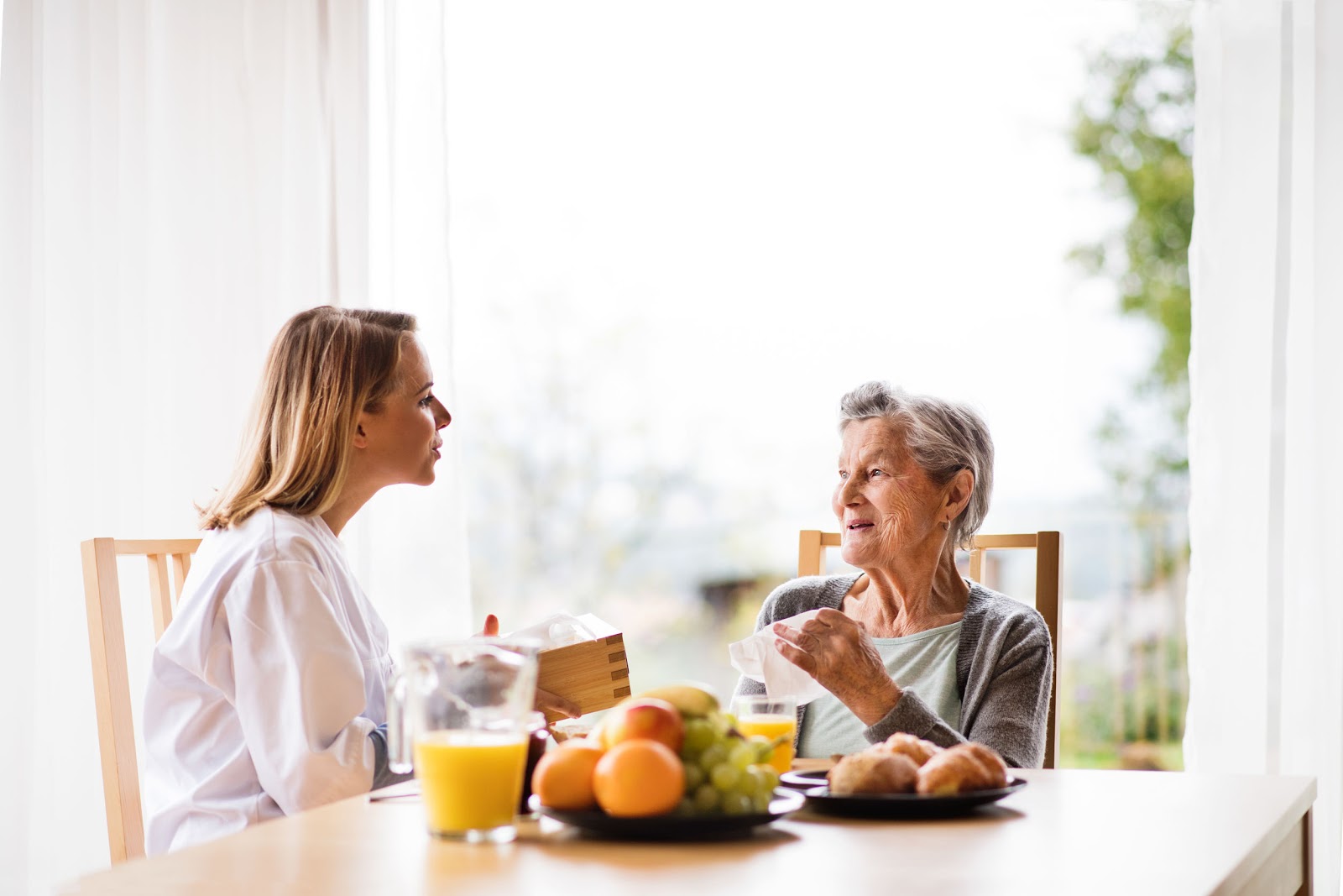 Health visitor and a senior woman during home visit. A nurse and an elderly woman sitting at the table, talking together.