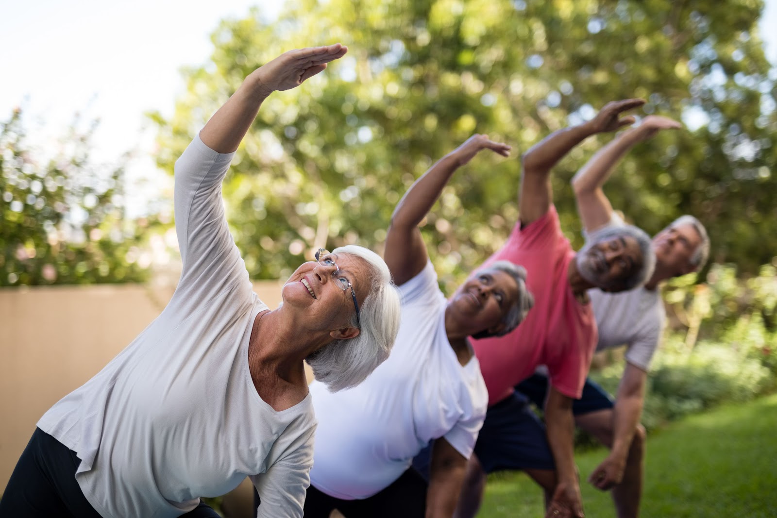 Senior people looking up while exercising with arms raised at park