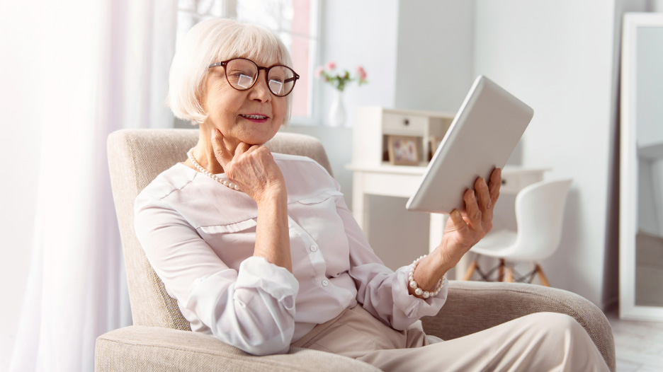 Senior woman looking at ipad sitting in a chair