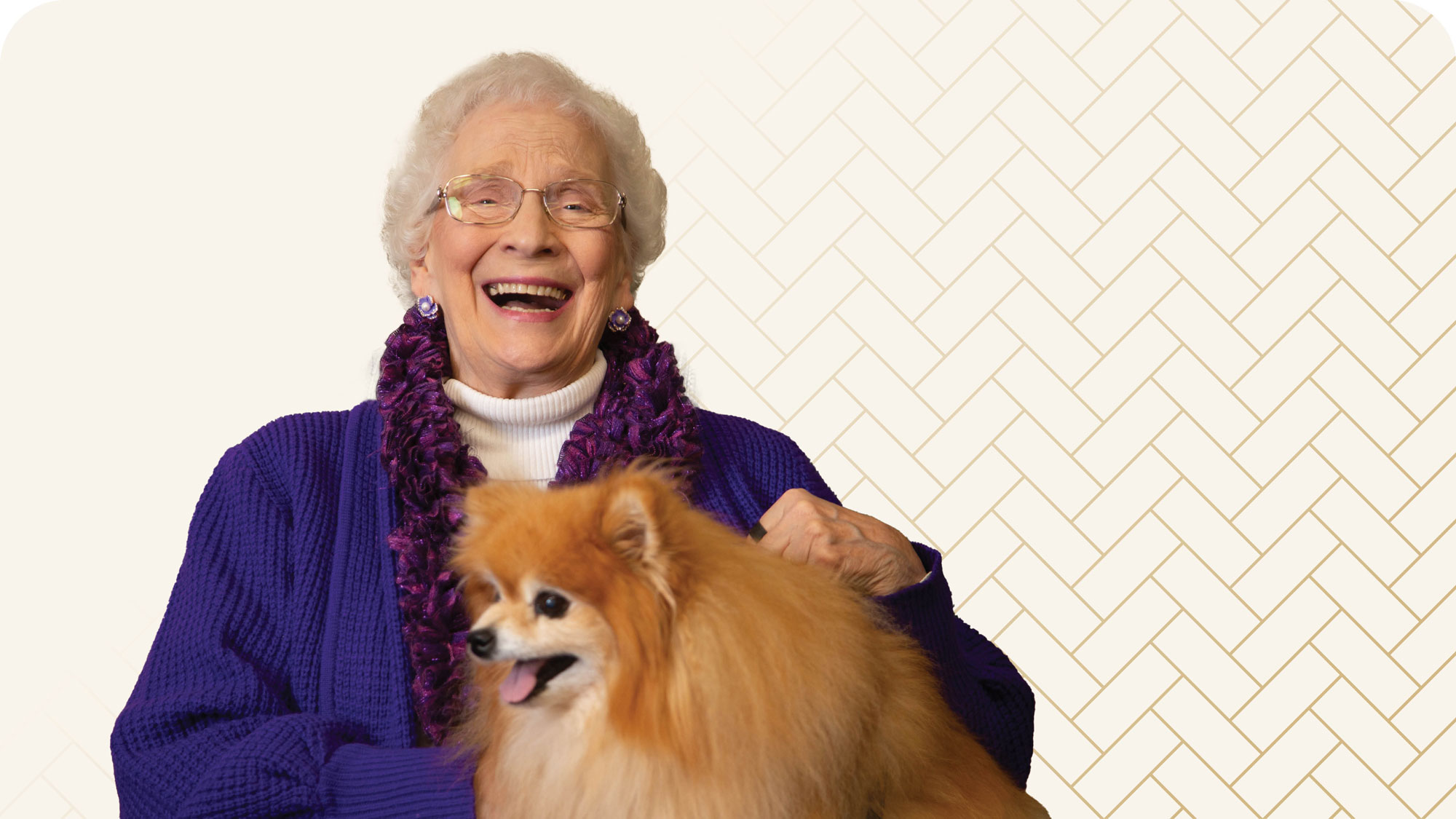 Elderly woman wearing glasses and a purple sweater, smiling widely while holding a fluffy Pomeranian dog. The background features a subtle, light herringbone pattern.