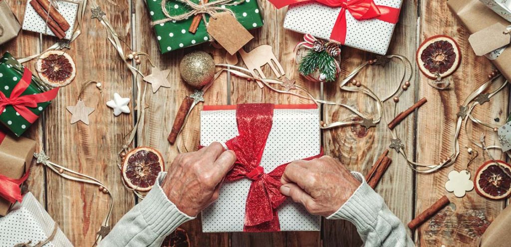 Elderly senior man's hands packing Christmas gifts on table with