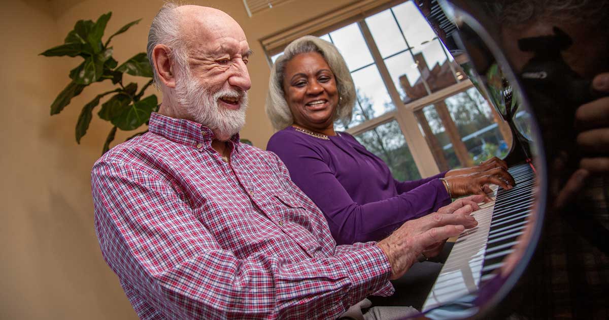 Senior resident playing piano with staff member