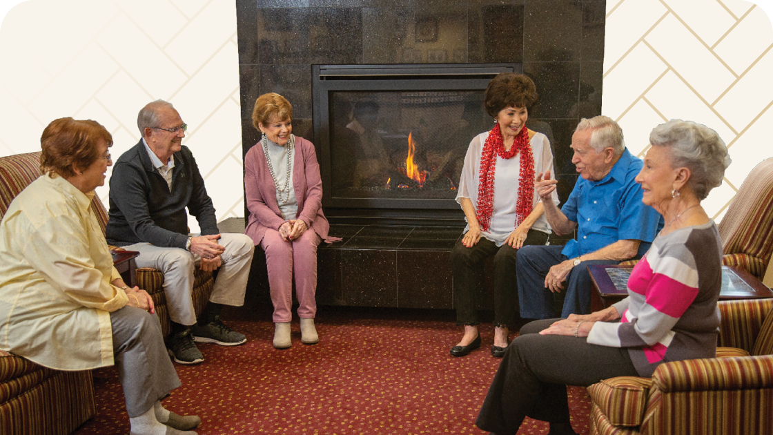 Group of seniors sitting in chairs in a circle by fireplace