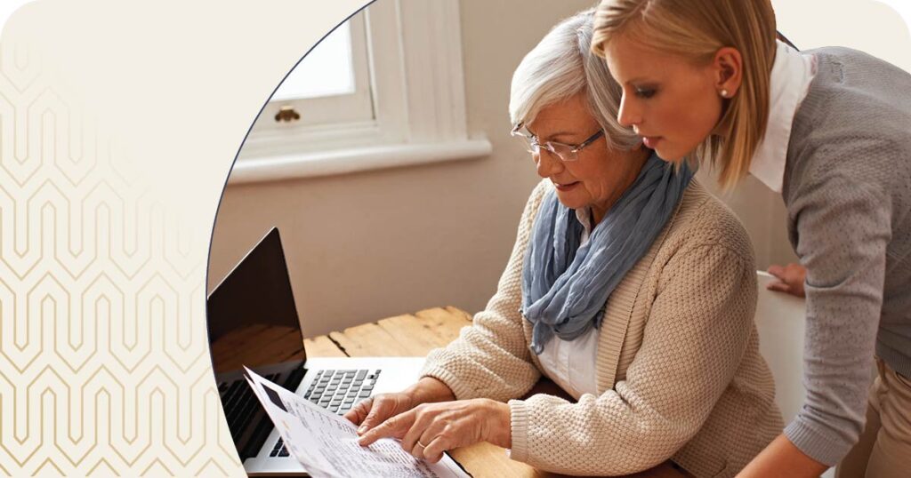 Senior woman and daughter reviewing paperwork at desk with computer