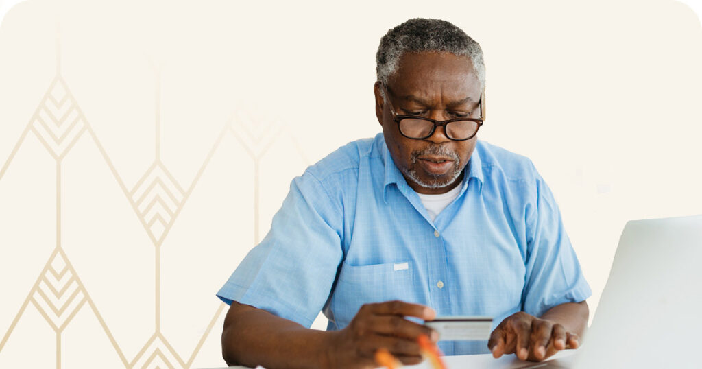 Senior man looking at a card while working on computer