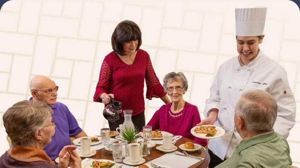 Staff member and a chef serving a group of seniors a meal