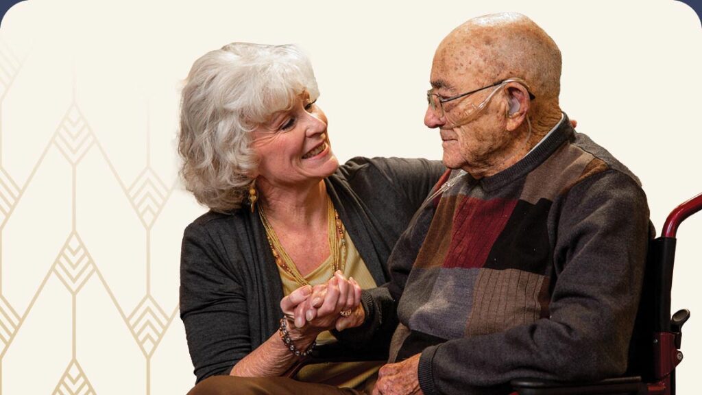 Senior woman holding senior man in wheelchair's hand