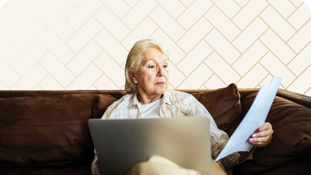 Senior woman sitting on couch with laptop and reviewing paperwork