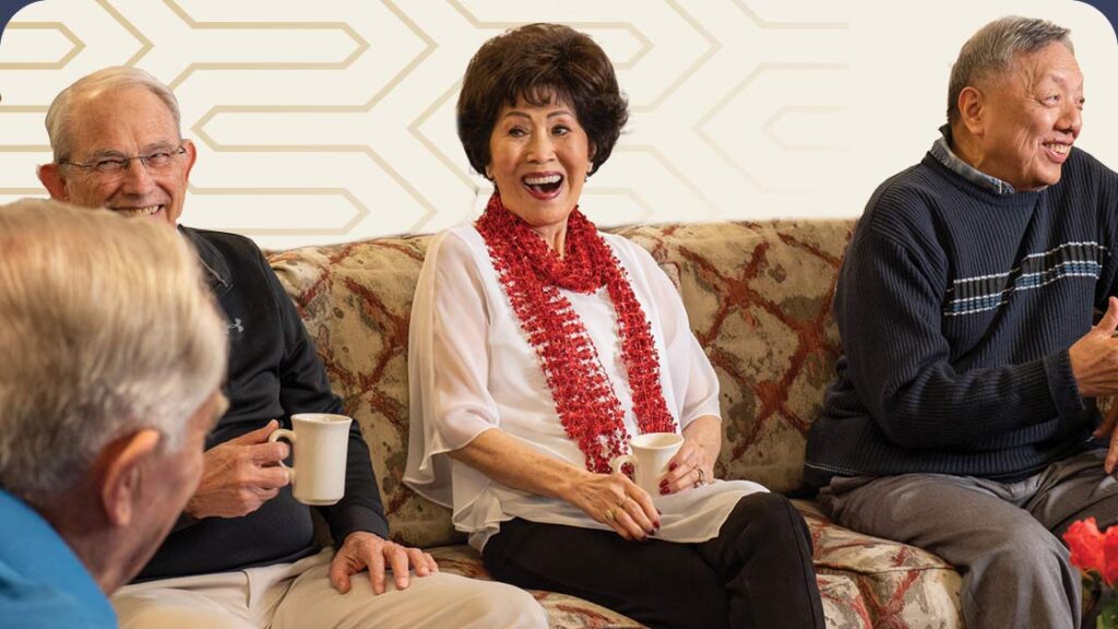 Seniors sitting on couch smiling, visiting and drinking coffee