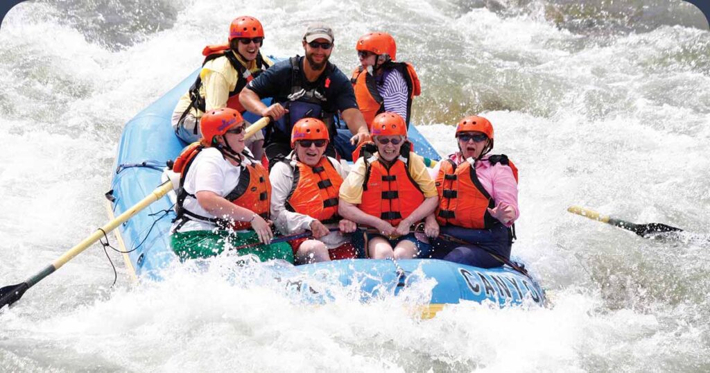 Group of seniors with life jackets and helmets white water rafting with guide
