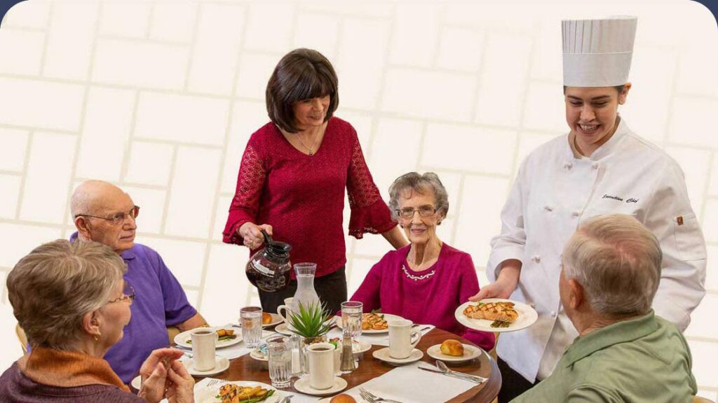 Staff member and chef serving seniors at dining table