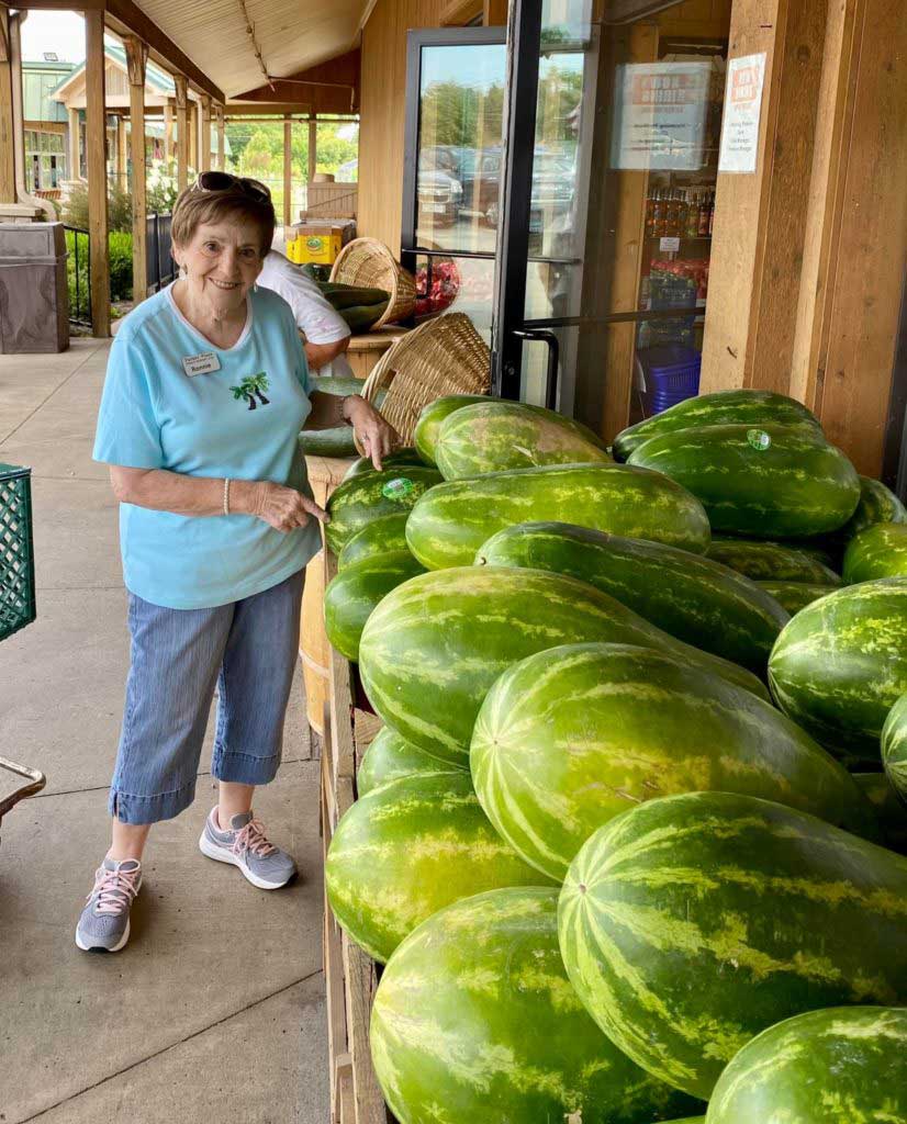 Senior resident standing next to a pile of watermelons