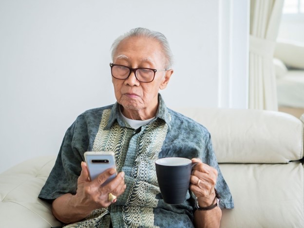 Senior looking at cellphone and drinking coffee