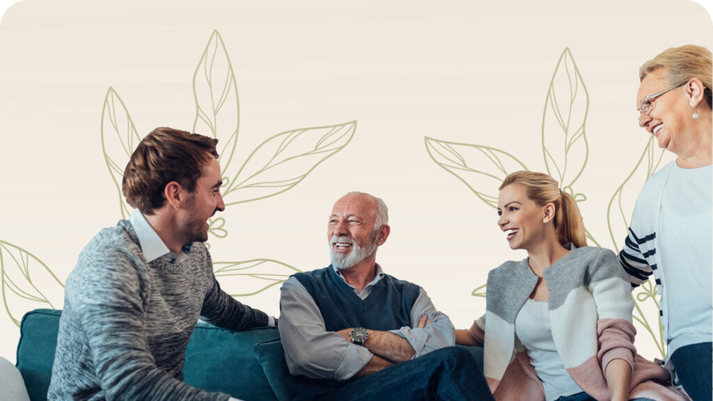 Four people are sitting on a couch, smiling and interacting. The group includes a younger man and woman, an older man with a beard, and an older woman wearing glasses. The background features a decorative leaf pattern.